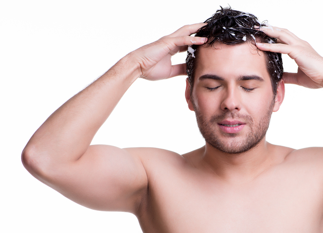 Young happy smiling man washing hair with closed eyes  - isolated on white.